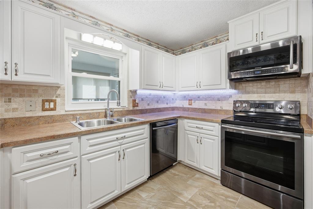 A kitchen with white cabinets, stainless steel appliances, tan countertops, and a tiled backsplash — 8350 SW 93RD LANE UNIT D, OCALA, FL