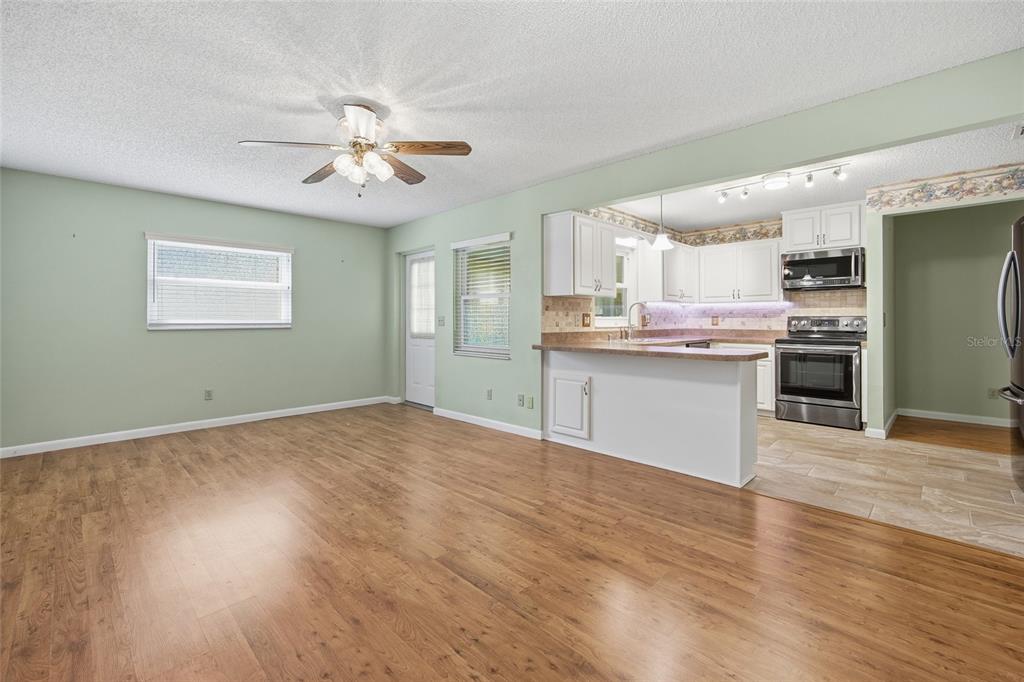 A living room with wood-look flooring opens to a kitchen featuring white cabinets and appliances — 8350 SW 93RD LANE UNIT D, OCALA, FL