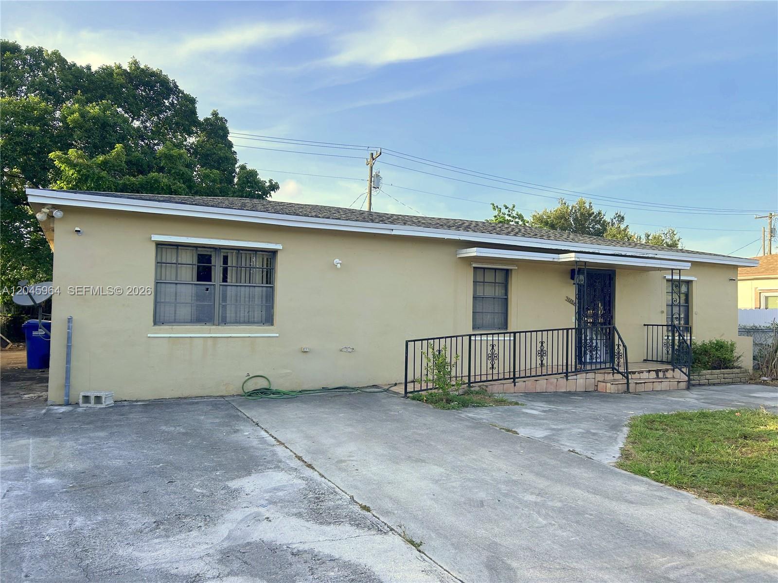 A single-story house with a beige stucco exterior, a concrete driveway, and a metal railing — 1355 NW 86th St, Miami FL 33147, MIAMI, FL