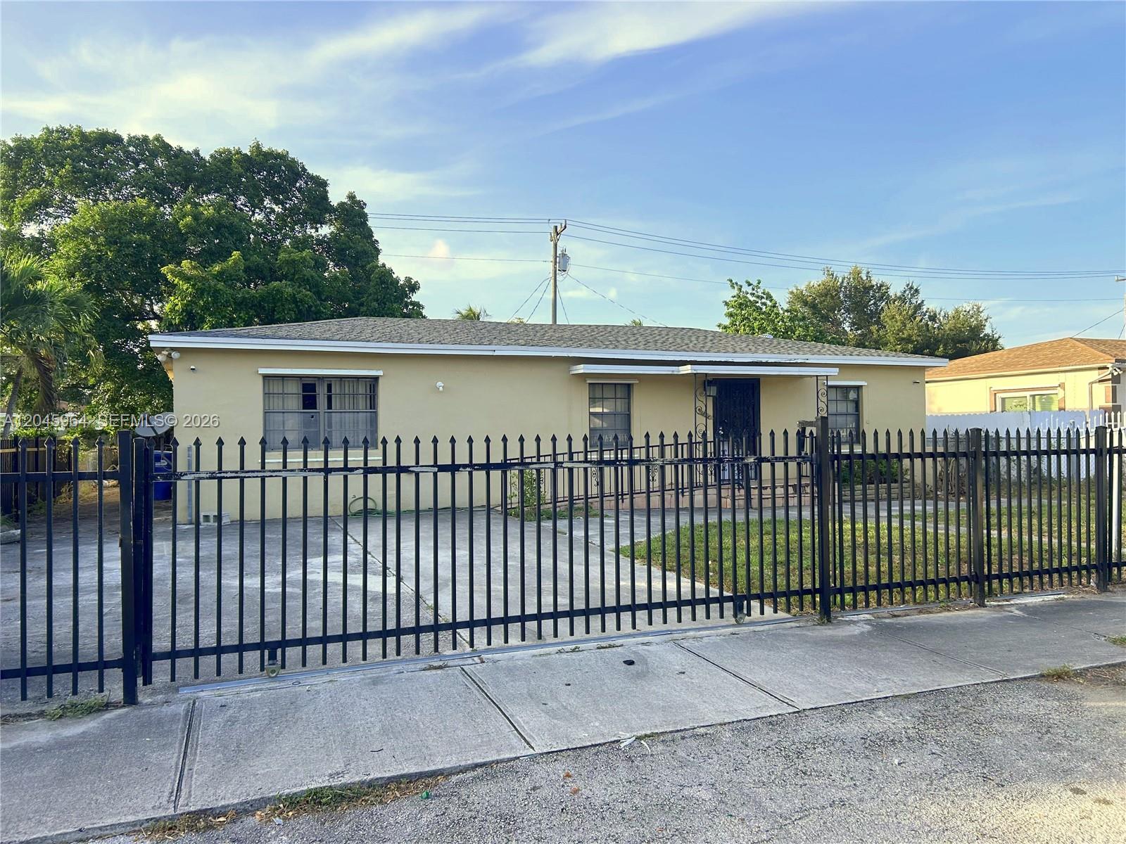A single-story yellow house with a black metal fence sits behind a concrete driveway — 1355 NW 86th St, Miami FL 33147, MIAMI, FL
