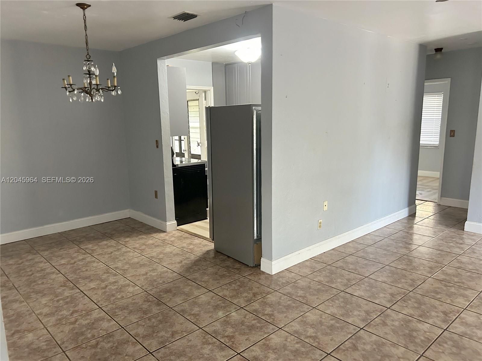 A dining area with a chandelier leads into a kitchen featuring a stainless steel refrigerator — 1355 NW 86th St, Miami FL 33147, MIAMI, FL