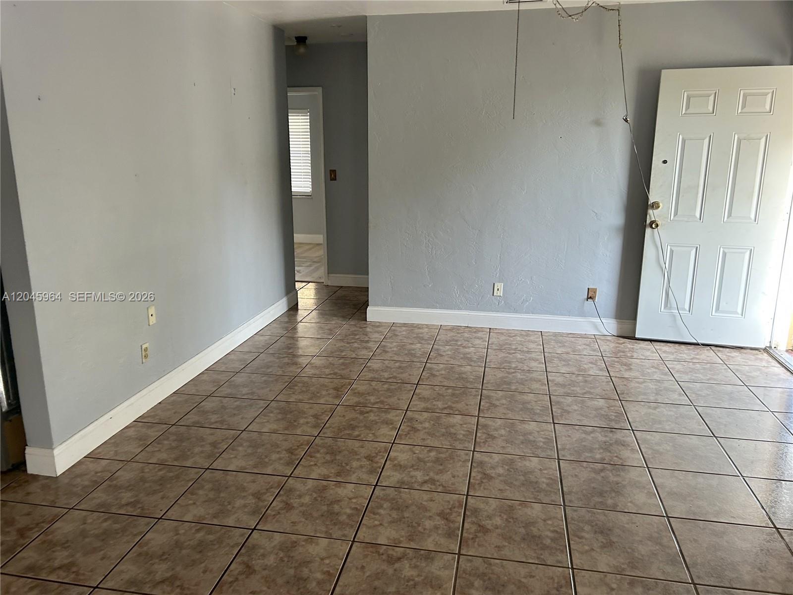 An empty room features gray walls, brown tiled flooring, and a white paneled door — 1355 NW 86th St, Miami FL 33147, MIAMI, FL