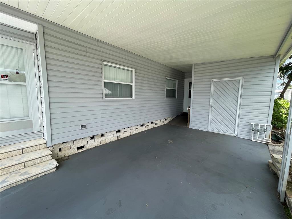 A covered carport area with gray siding, a storage door, and a concrete foundation — 140 MOUNTAIN FIR DRIVE, PALM HARBOR, FL
