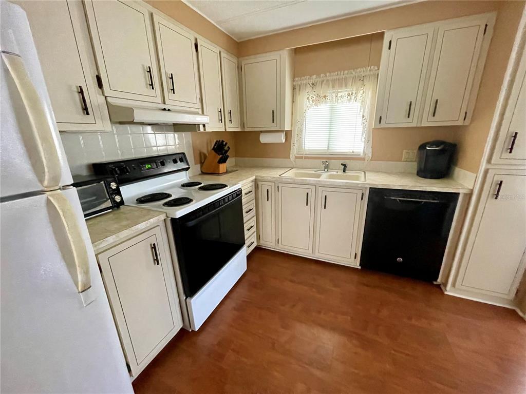 A kitchen features white cabinets, black appliances, a double sink, and wood-look flooring — 140 MOUNTAIN FIR DRIVE, PALM HARBOR, FL
