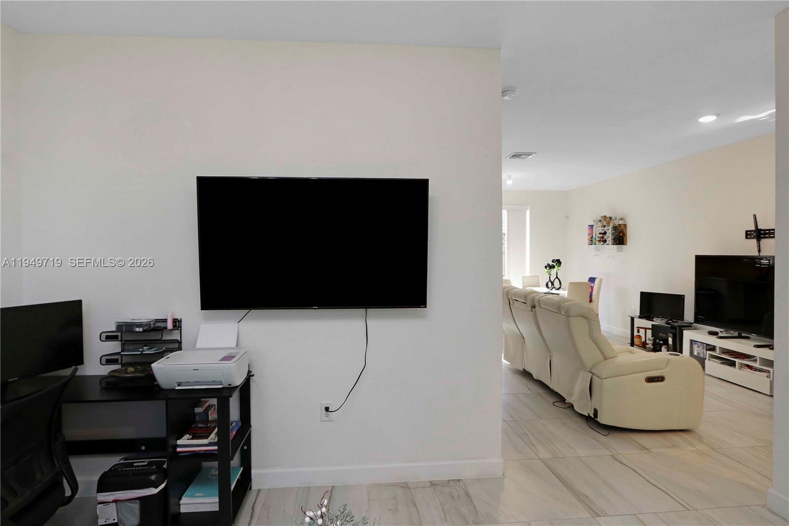 A wall-mounted television hangs above a desk in a room adjacent to a living area — 2432 SE 10th Ct, Homestead FL 33035, HOMESTEAD, FL