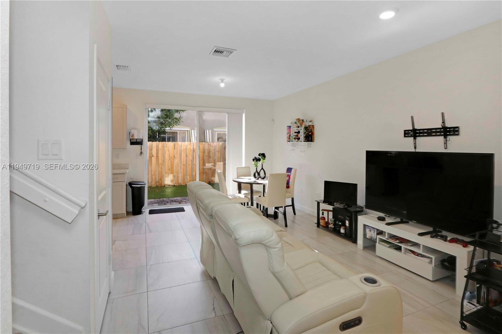 A living room with white tile floors, a white sofa, and a sliding glass door — 2432 SE 10th Ct, Homestead FL 33035, HOMESTEAD, FL