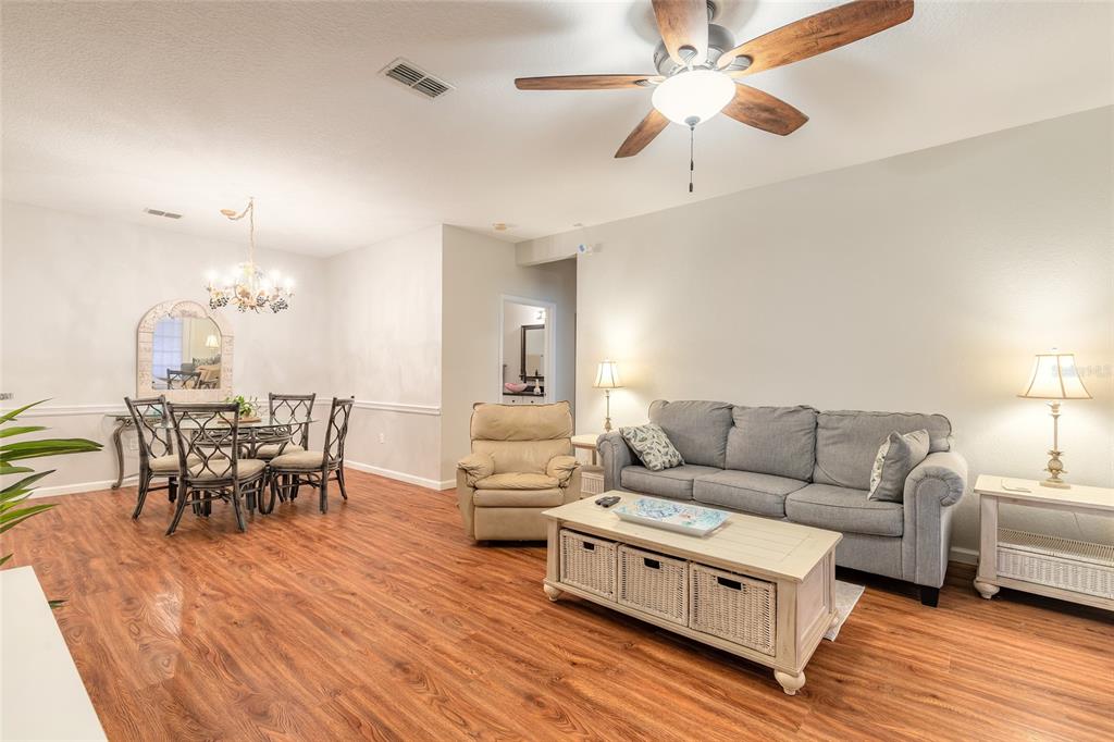 A living and dining room area with wood-look flooring, a ceiling fan, and neutral walls — 830 AIRPORT ROAD UNIT 105, PORT ORANGE, FL