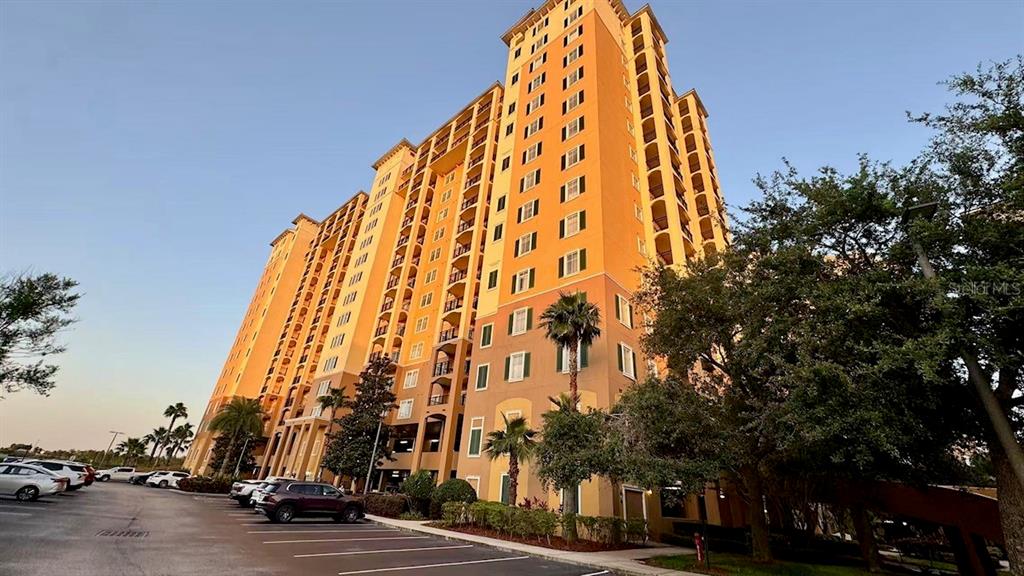 A tall, multi-story orange apartment building stands next to a parking lot with several cars — 8125 RESORT VILLAGE DRIVE UNIT 5808, ORLANDO, FL