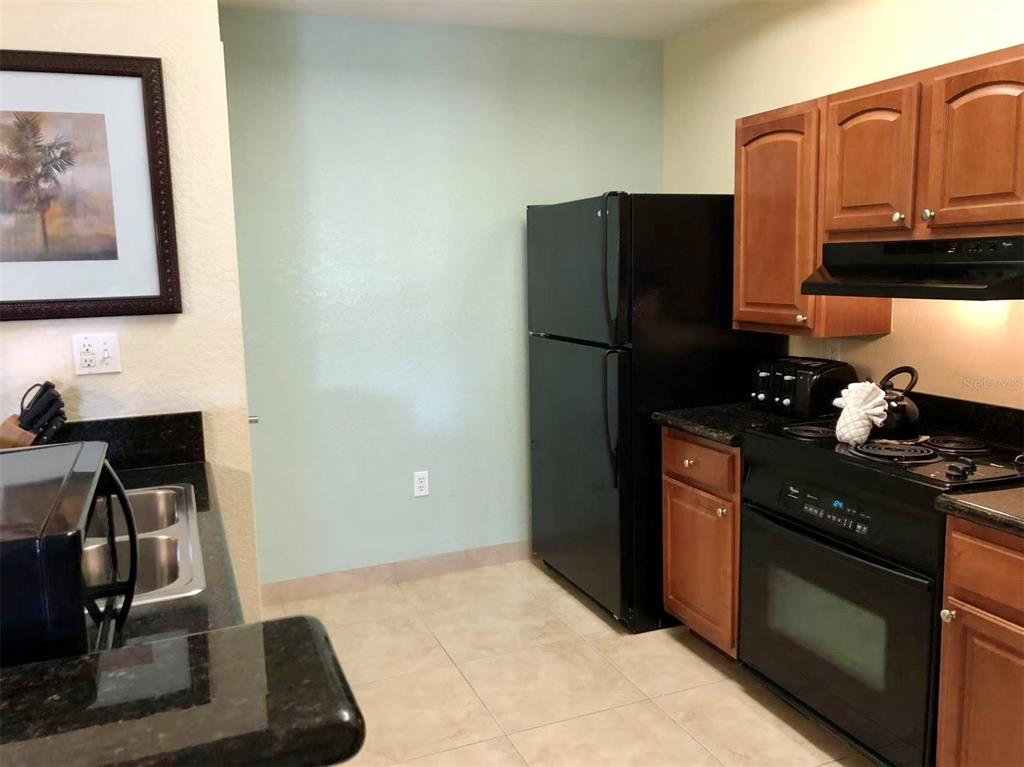 A kitchen features black appliances, wood cabinets, dark countertops, and light green walls — 8125 RESORT VILLAGE DRIVE UNIT 5808, ORLANDO, FL