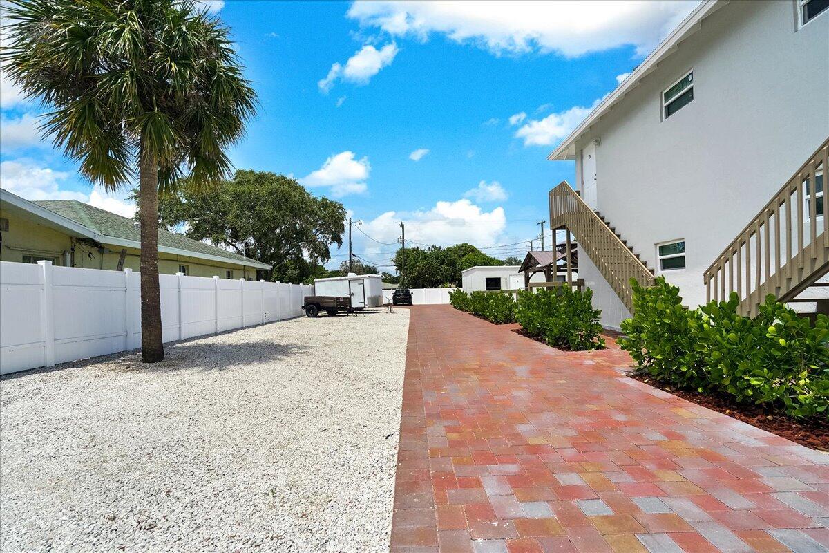 A gravel parking area sits beside a brick paver walkway and a white building exterior — 305 Cypress Drive E # 5, Lake Park FL 33403, LAKE PARK, FL