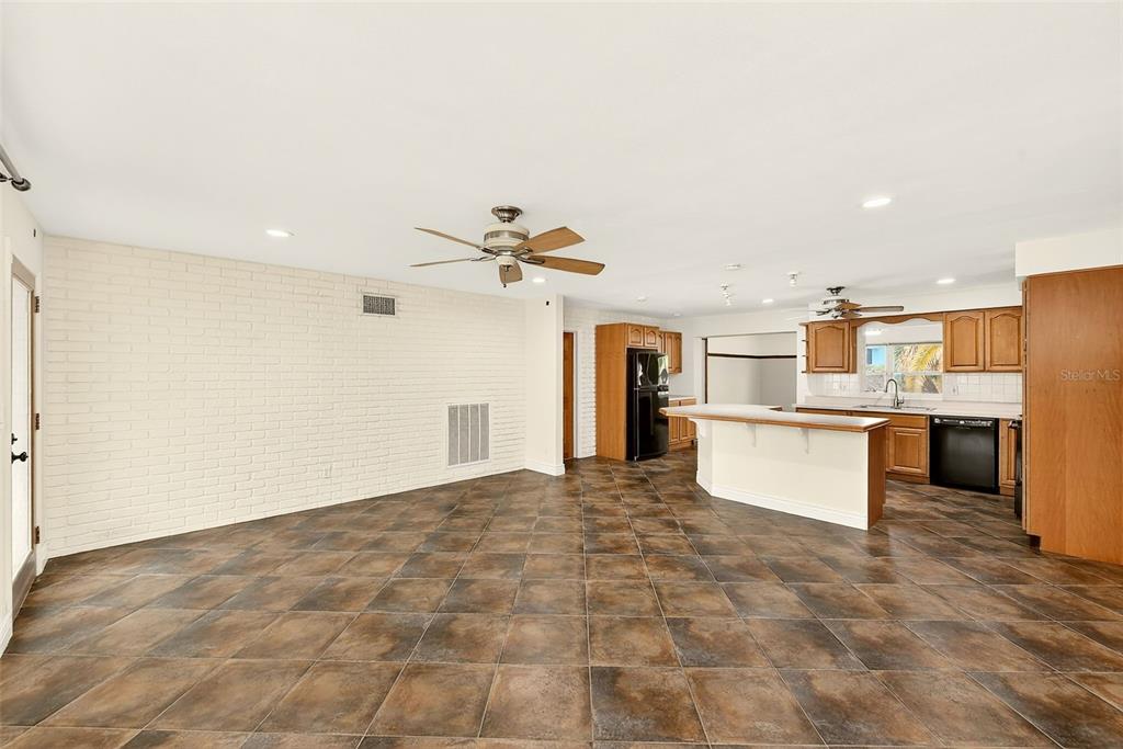 An open-concept kitchen and living area features tile flooring, a brick wall, and wood cabinets — 1465 BAYVIEW DRIVE, CLEARWATER, FL