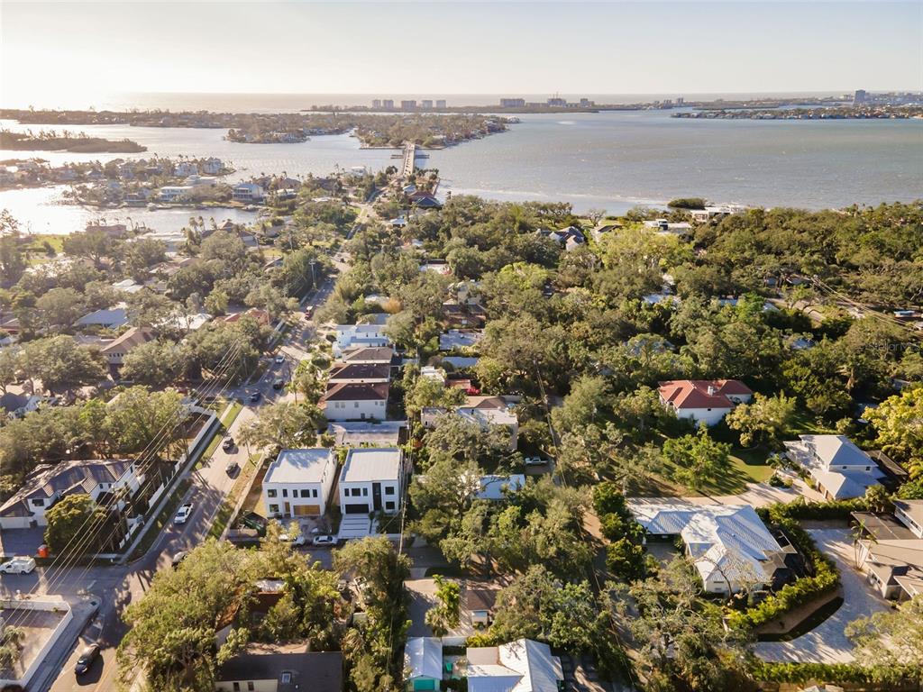 An aerial view shows a coastal neighborhood with houses, dense trees, and a distant bridge — 1704 WISCONSIN LANE, SARASOTA, FL