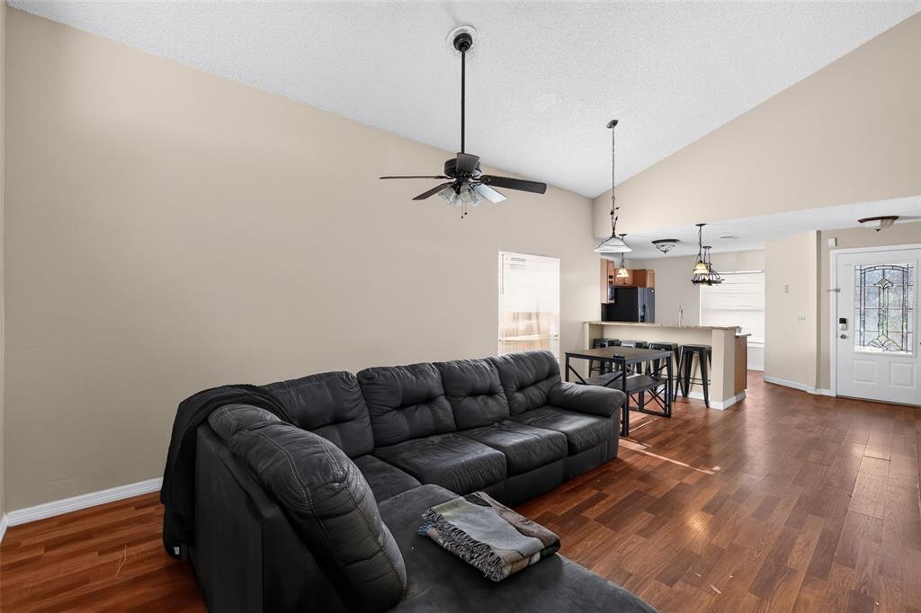 A living room with a large sectional sofa, hardwood floors, and an open kitchen area — 1243 PIN OAK DRIVE, APOPKA, FL