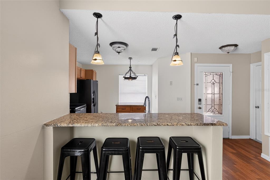 A kitchen features a granite breakfast bar with four black stools and pendant lighting — 1243 PIN OAK DRIVE, APOPKA, FL