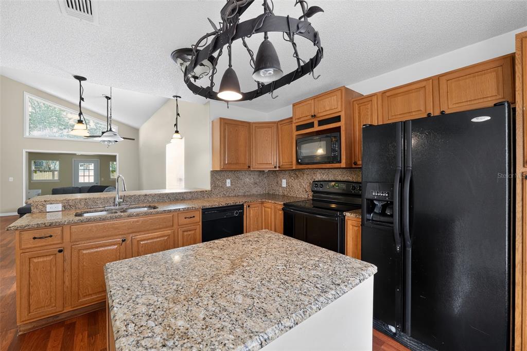 A kitchen features oak cabinets, granite countertops, black appliances, and a central island — 1243 PIN OAK DRIVE, APOPKA, FL