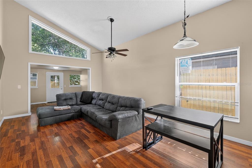 A living room features a vaulted ceiling, dark wood flooring, a sectional sofa, and windows — 1243 PIN OAK DRIVE, APOPKA, FL