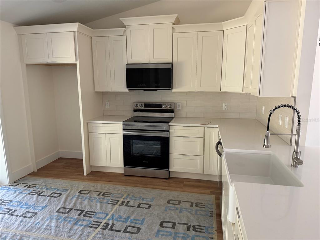 A kitchen features white cabinets, stainless steel appliances, a farmhouse sink, and light countertops — 64 EMERSON DRIVE, PALM COAST, FL