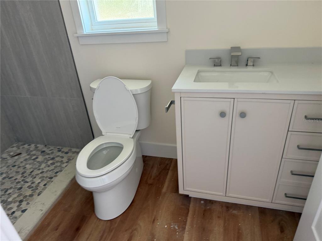 A bathroom features a white vanity, a toilet, and a walk-in shower with pebble flooring — 64 EMERSON DRIVE, PALM COAST, FL
