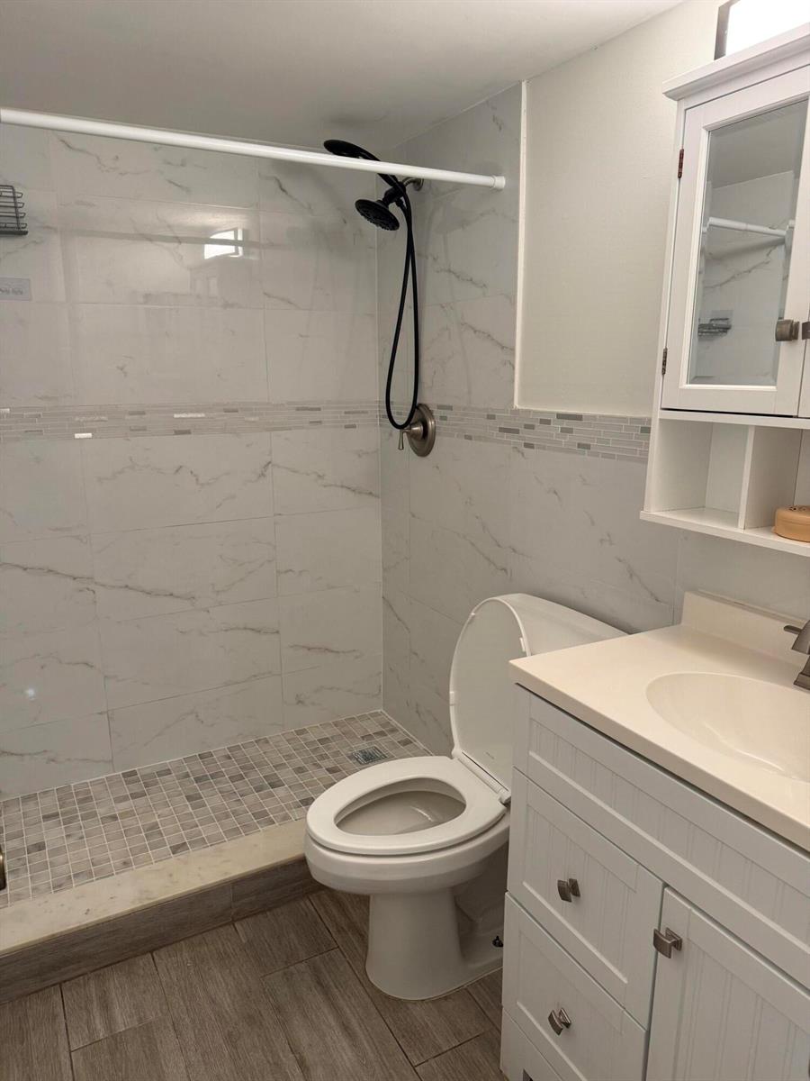 A bathroom features a walk-in shower with marble-look tiles, a toilet, and a white vanity — 255 S Cypress Road # 339, Pompano Beach FL 33060, POMPANO BEACH, FL