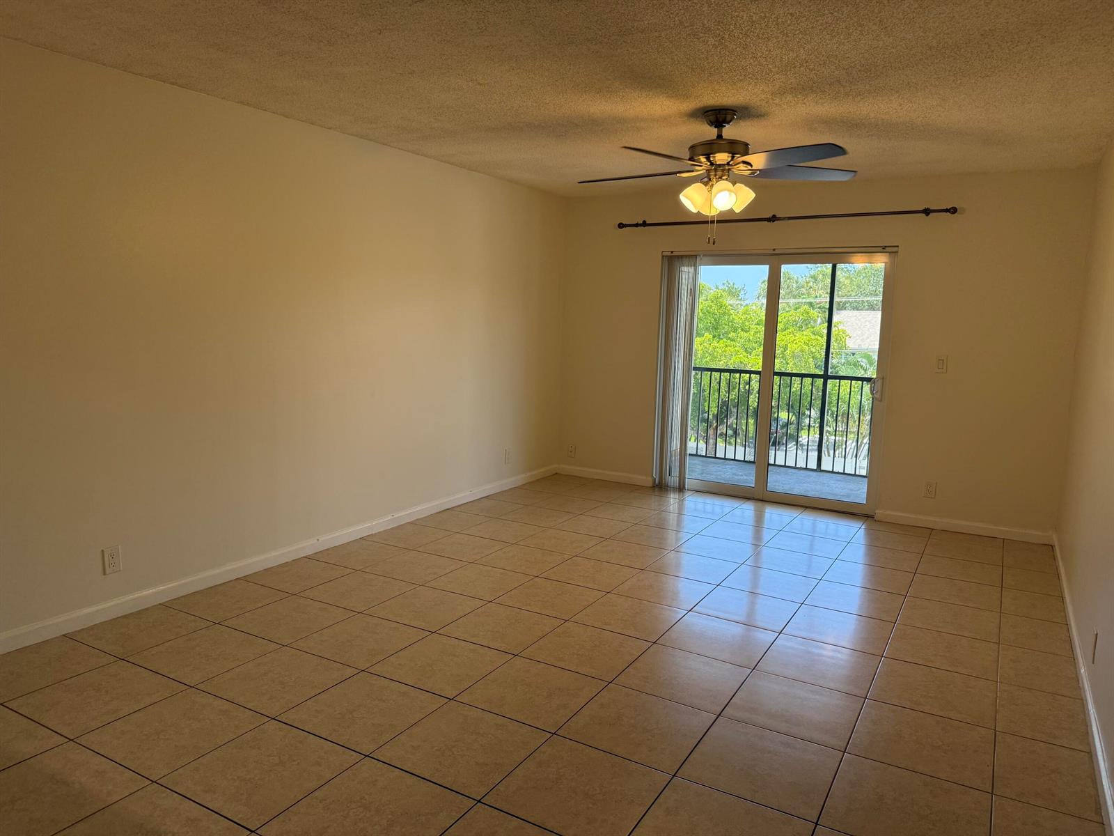 An empty living room features beige tile flooring, a ceiling fan, and sliding glass balcony doors — 255 S Cypress Road # 339, Pompano Beach FL 33060, POMPANO BEACH, FL