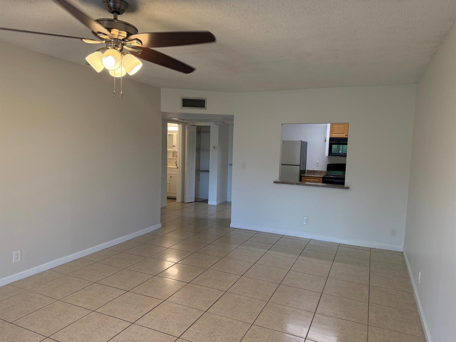 An empty room with beige tile flooring, a ceiling fan, and a kitchen pass-through window — 255 S Cypress Road # 339, Pompano Beach FL 33060, POMPANO BEACH, FL