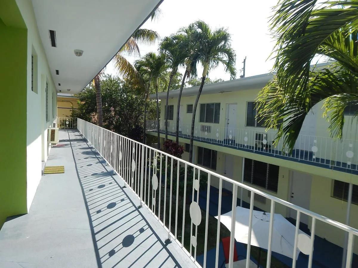 An elevated outdoor walkway overlooks a courtyard with palm trees and a two-story apartment building — 1200 Marseille Drive, Miami Beach FL 33141, MIAMI BEACH, FL