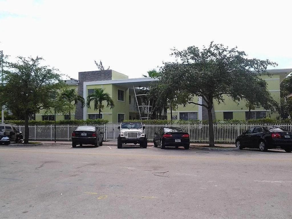 A light green apartment building with a white fence and parked cars in front — 1200 Marseille Drive, Miami Beach FL 33141, MIAMI BEACH, FL