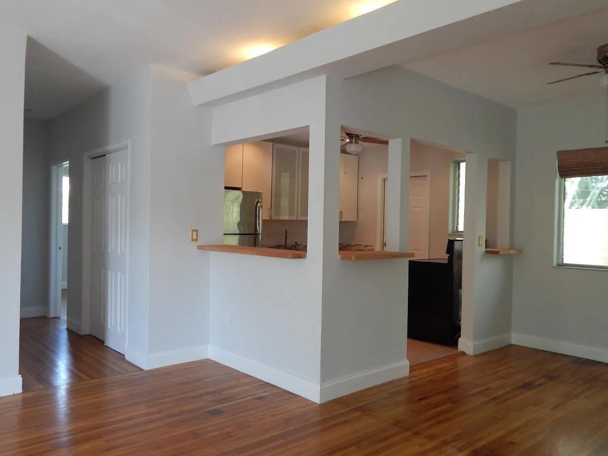 A living room with hardwood floors looks into a kitchen through two wall cutouts — 1200 Marseille Drive, Miami Beach FL 33141, MIAMI BEACH, FL