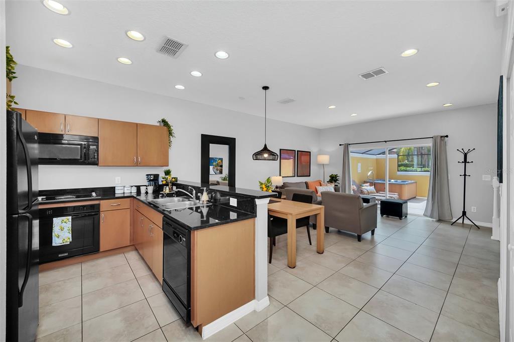 A kitchen with dark countertops and wood cabinets opens into a living and dining area — 3070 YELLOW LANTANA LANE, KISSIMMEE, FL