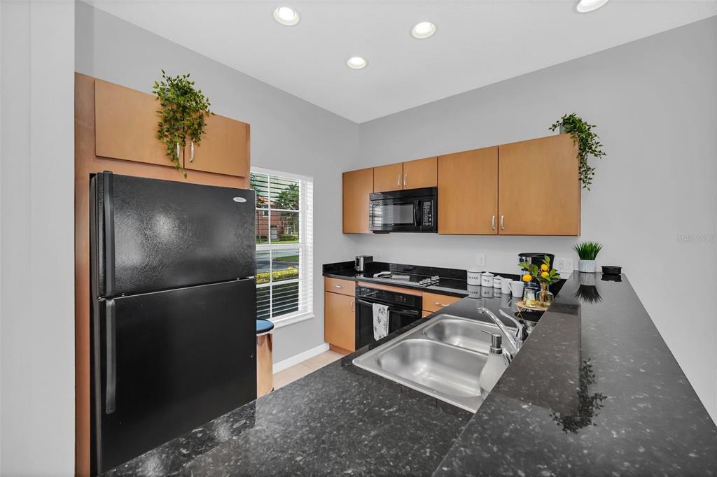 A kitchen features black countertops, light wood cabinets, a black refrigerator, and a double sink — 3070 YELLOW LANTANA LANE, KISSIMMEE, FL