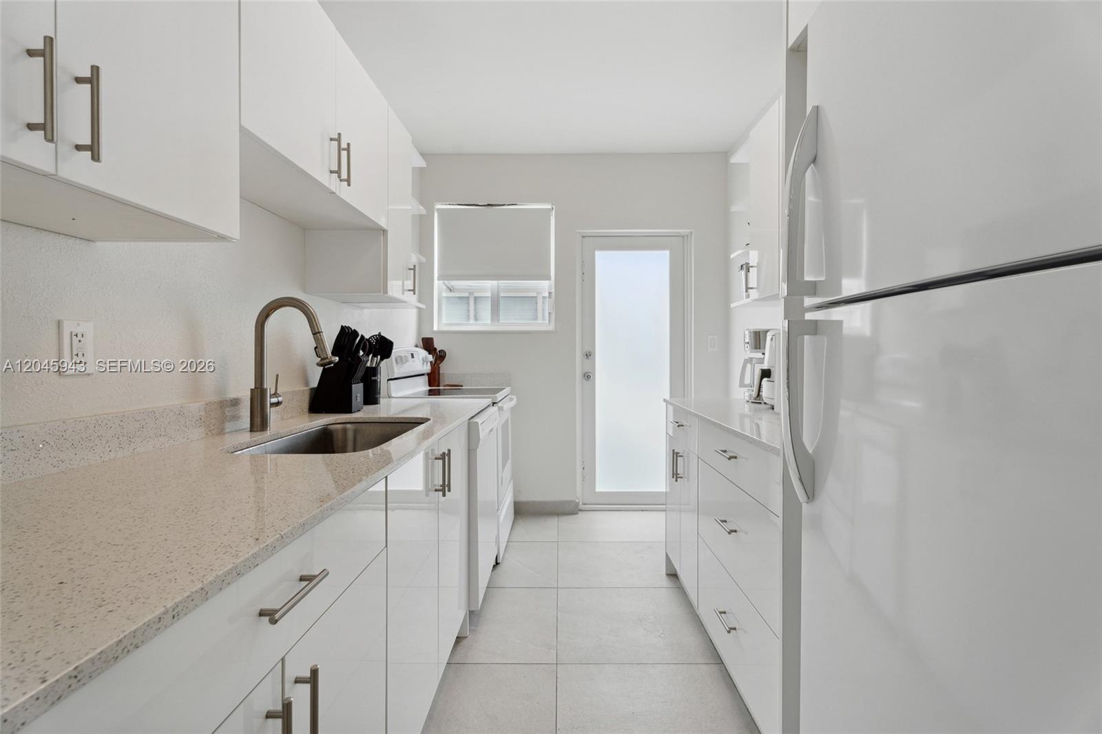 A galley-style kitchen features white cabinets, light countertops, stainless steel appliances, and tile flooring — 835 80th St # 3, Miami Beach FL 33141, MIAMI BEACH, FL