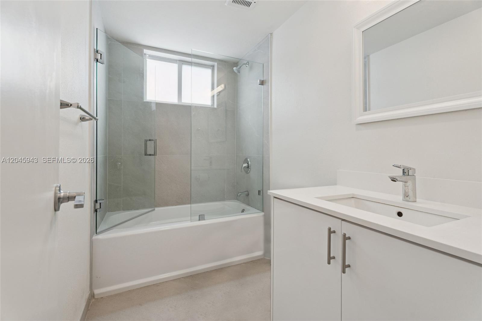 A bathroom features a white vanity, a glass-enclosed bathtub shower, and light-colored tile walls — 835 80th St # 3, Miami Beach FL 33141, MIAMI BEACH, FL