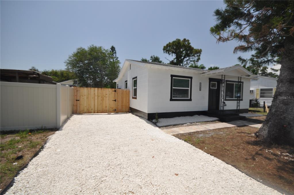 A white house with black trim features a gravel driveway and a wooden gate — 1319 S 56TH STREET, GULFPORT, FL