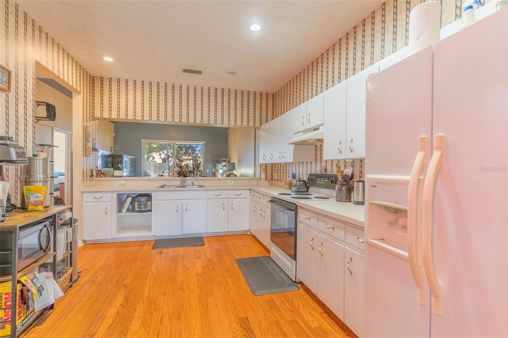 A kitchen features white cabinets, a pink refrigerator, wood flooring, and patterned wallpaper — 4317 DINNER LAKE DRIVE, LAKE WALES, FL