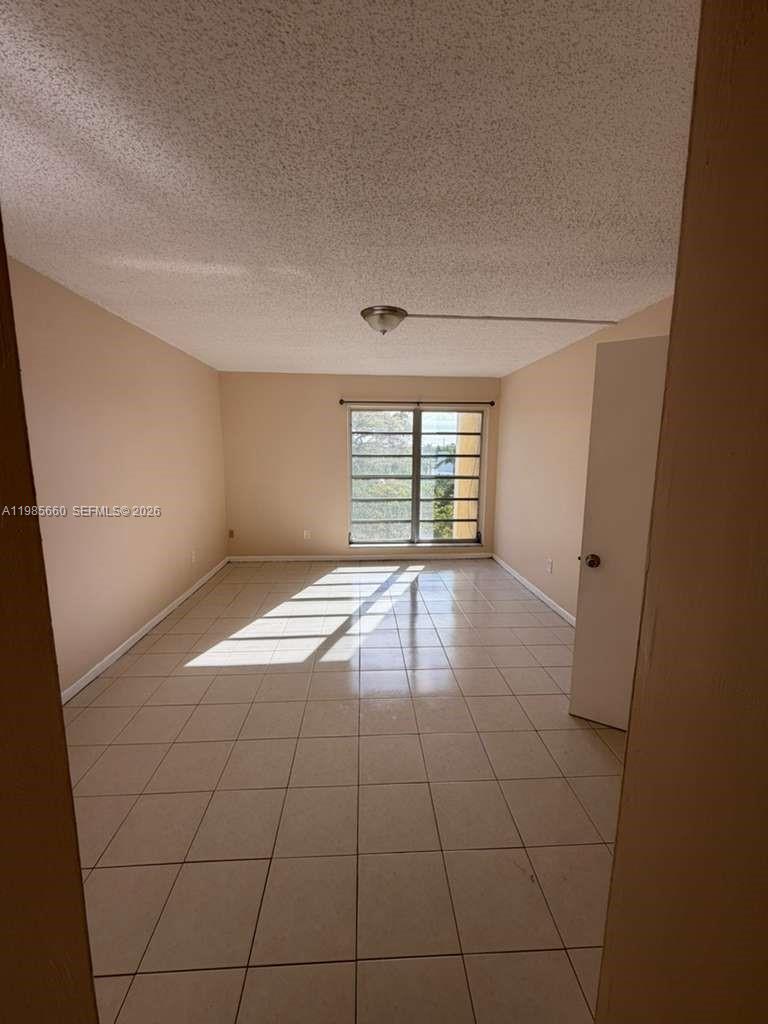 An empty bedroom features light-colored tile flooring, beige walls, and a single window — 9180 Fontainebleau Blvd # 401, Miami FL 33172, MIAMI, FL