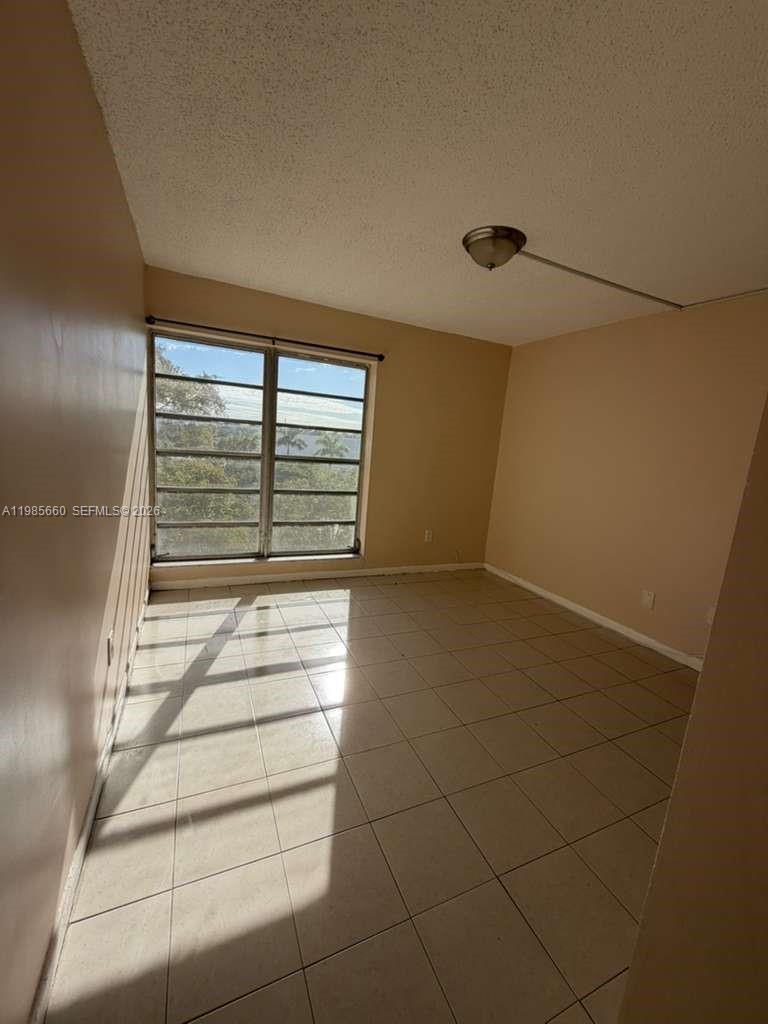 An empty room features beige walls, light-colored tile flooring, and a large window — 9180 Fontainebleau Blvd # 401, Miami FL 33172, MIAMI, FL