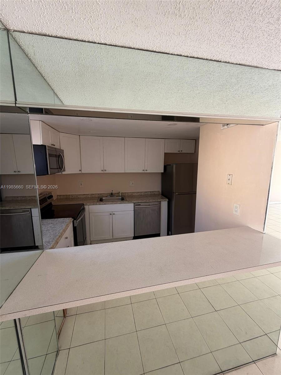 A kitchen features white cabinets, stainless steel appliances, and a breakfast bar with mirrored walls — 9180 Fontainebleau Blvd # 401, Miami FL 33172, MIAMI, FL