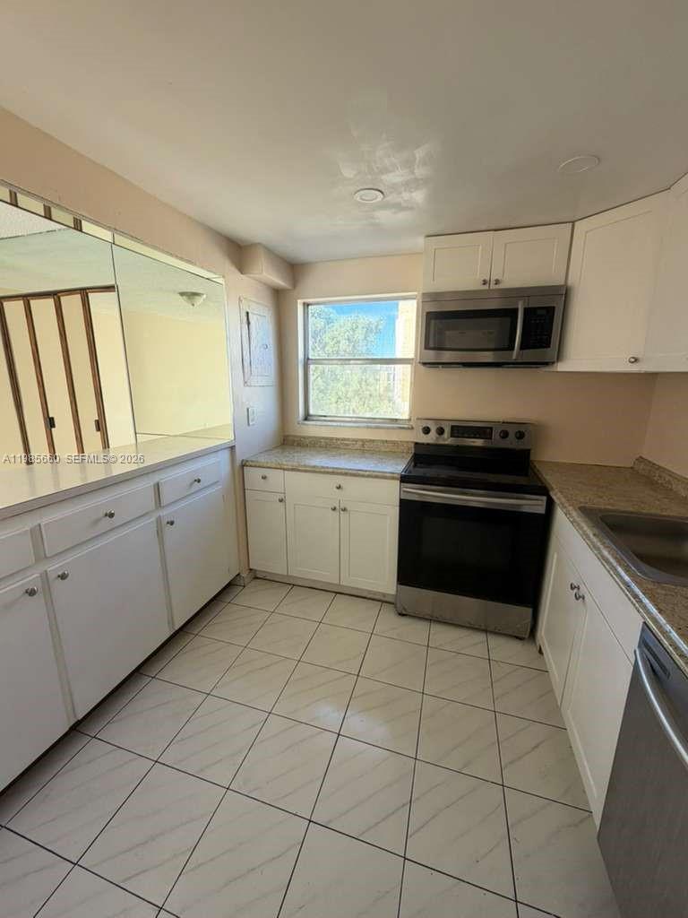 A kitchen features white cabinets, stainless steel appliances, tile flooring, and a large wall mirror — 9180 Fontainebleau Blvd # 401, Miami FL 33172, MIAMI, FL