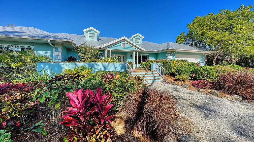 A light blue house with a metal roof features a gravel driveway and lush landscaping — 1440 KIMLIRA LANE, SARASOTA, FL