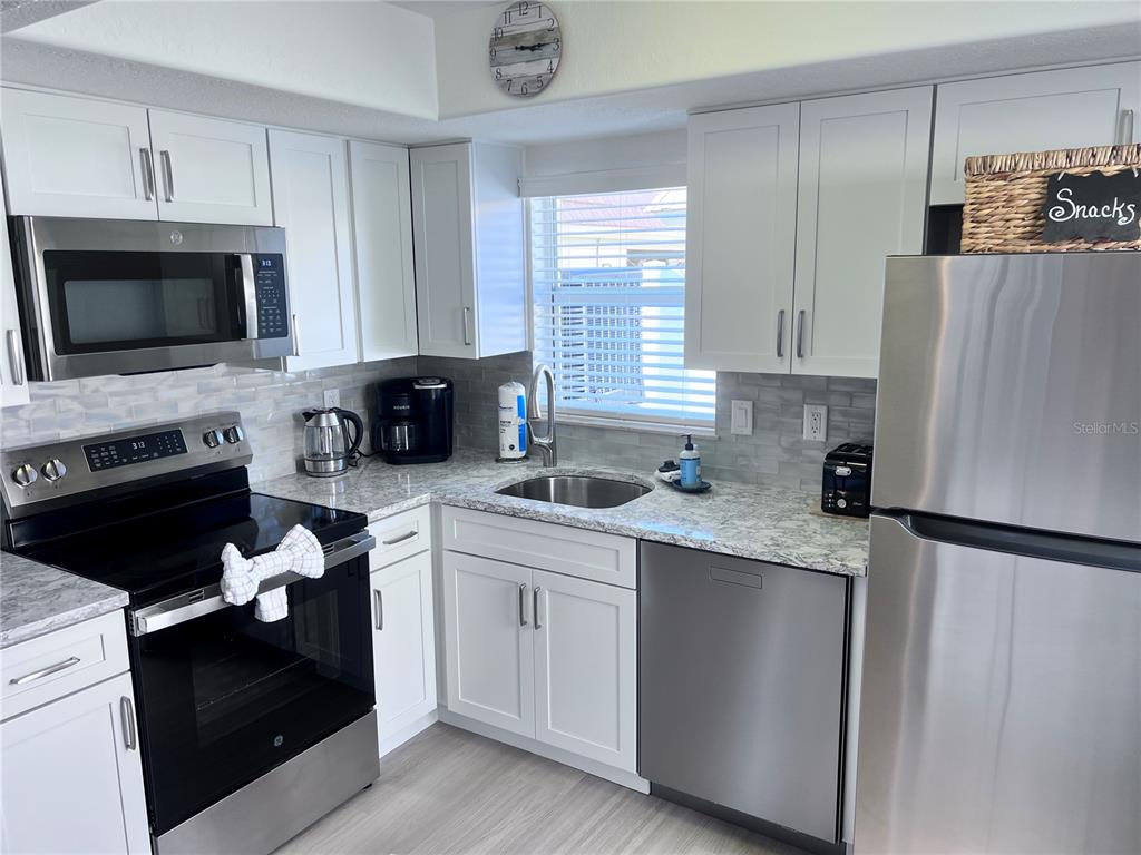 A kitchen features white cabinets, stainless steel appliances, granite countertops, and a subway tile backsplash — 6154 MIDNIGHT PASS ROAD UNIT A11, SARASOTA, FL