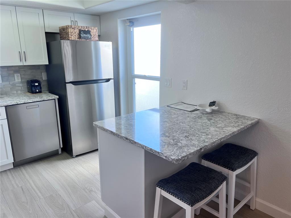 A kitchen features white cabinets, stainless steel appliances, and a granite-topped island with two stools — 6154 MIDNIGHT PASS ROAD UNIT A11, SARASOTA, FL