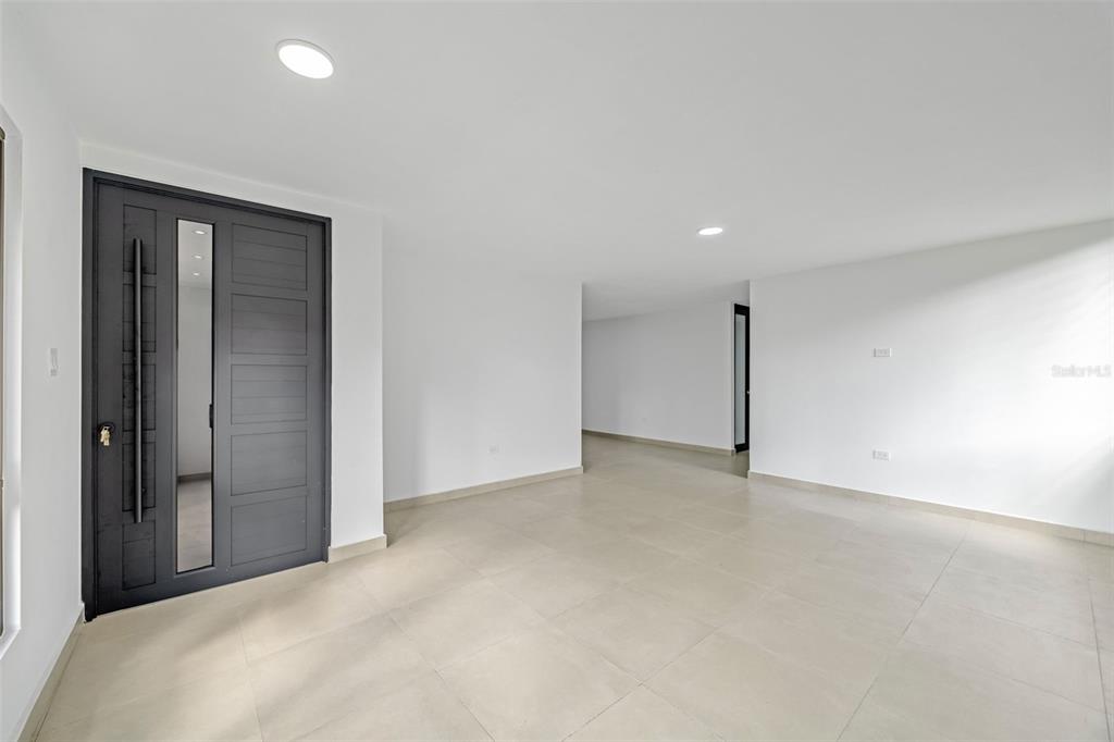 An interior view of a room with white walls, tiled floors, and a dark door — RAMON MARIN ST. LEVITTOWN LAKES UNIT EA-34, TOA BAJA, PR