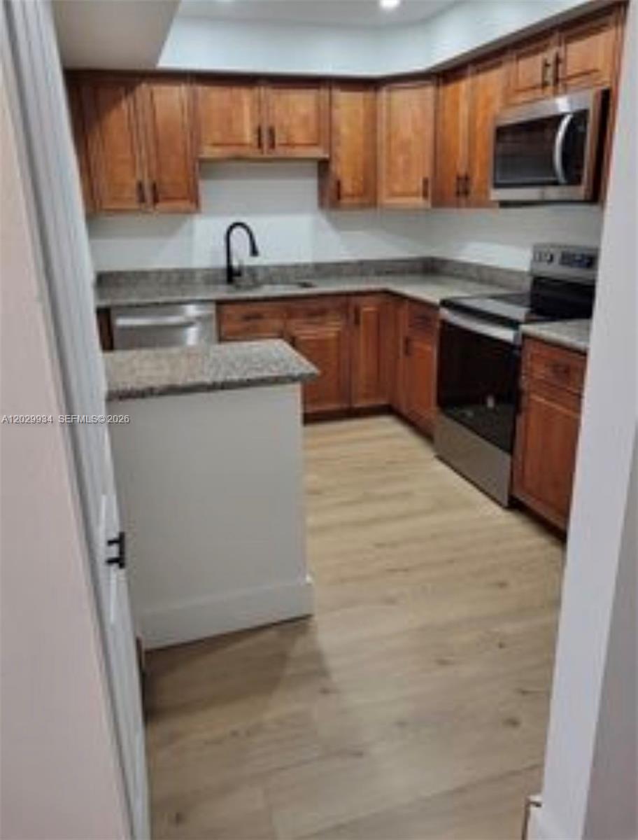 A kitchen features wood cabinets, granite countertops, stainless steel appliances, and light wood flooring — 733 SE 1st Way # 109, Deerfield Beach FL 33441, DEERFIELD BEACH, FL