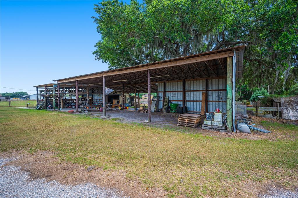 A large, open-sided metal pole barn sits on a grassy lot under a large tree — 1616 MCGEE ROAD, PLANT CITY, FL