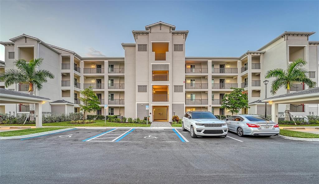 A multi-story apartment building with a parking lot and two cars in the foreground — 12140 WELLEN GOLF STREET UNIT 301, VENICE, FL