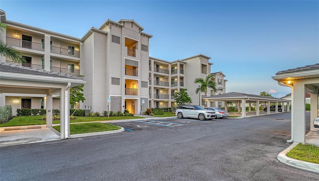 A multi-story apartment building with covered parking spaces and a paved driveway in front — 12140 WELLEN GOLF STREET UNIT 301, VENICE, FL