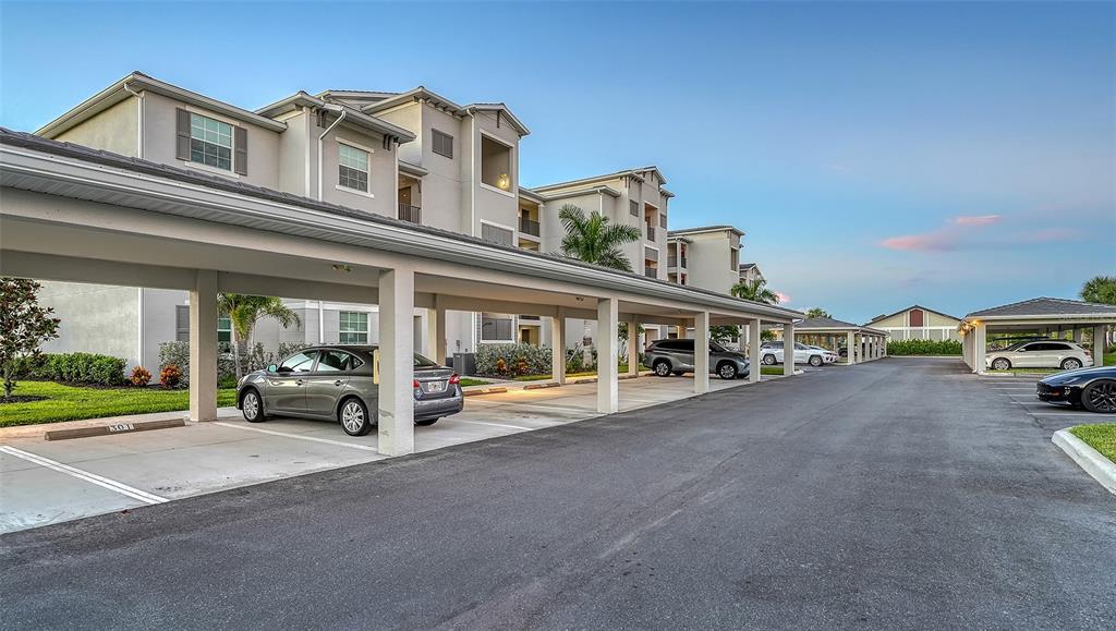 A multi-story apartment building with covered parking spaces and several parked cars — 12140 WELLEN GOLF STREET UNIT 301, VENICE, FL