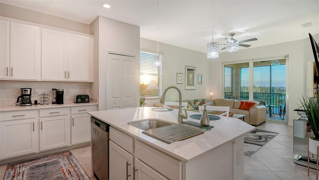 A kitchen with white cabinets and a center island overlooks a living room and balcony — 12140 WELLEN GOLF STREET UNIT 301, VENICE, FL