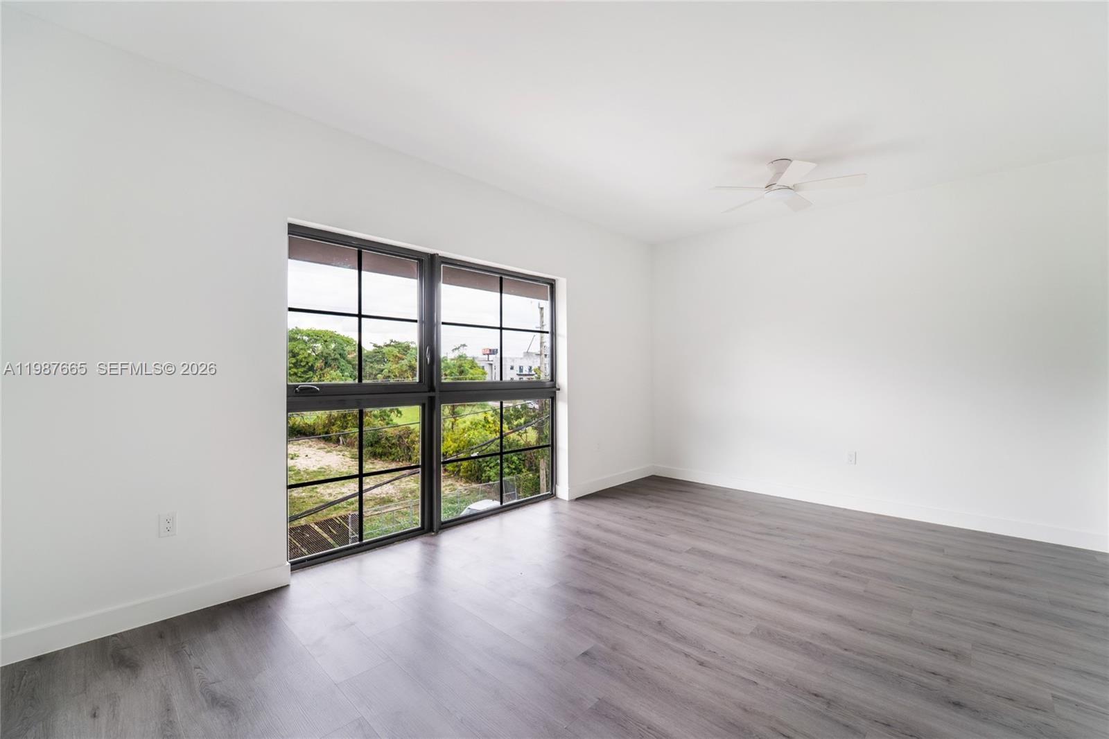 An empty room features white walls, gray wood-look flooring, a ceiling fan, and grid-pane windows — 1165 NW 8th Ave # 101, Miami FL 33136, MIAMI, FL