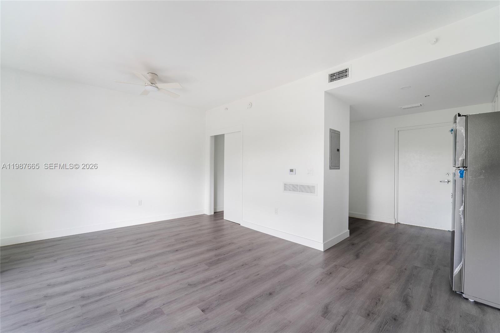 An empty room features white walls, dark wood-look flooring, a ceiling fan, and a refrigerator — 1165 NW 8th Ave # 101, Miami FL 33136, MIAMI, FL